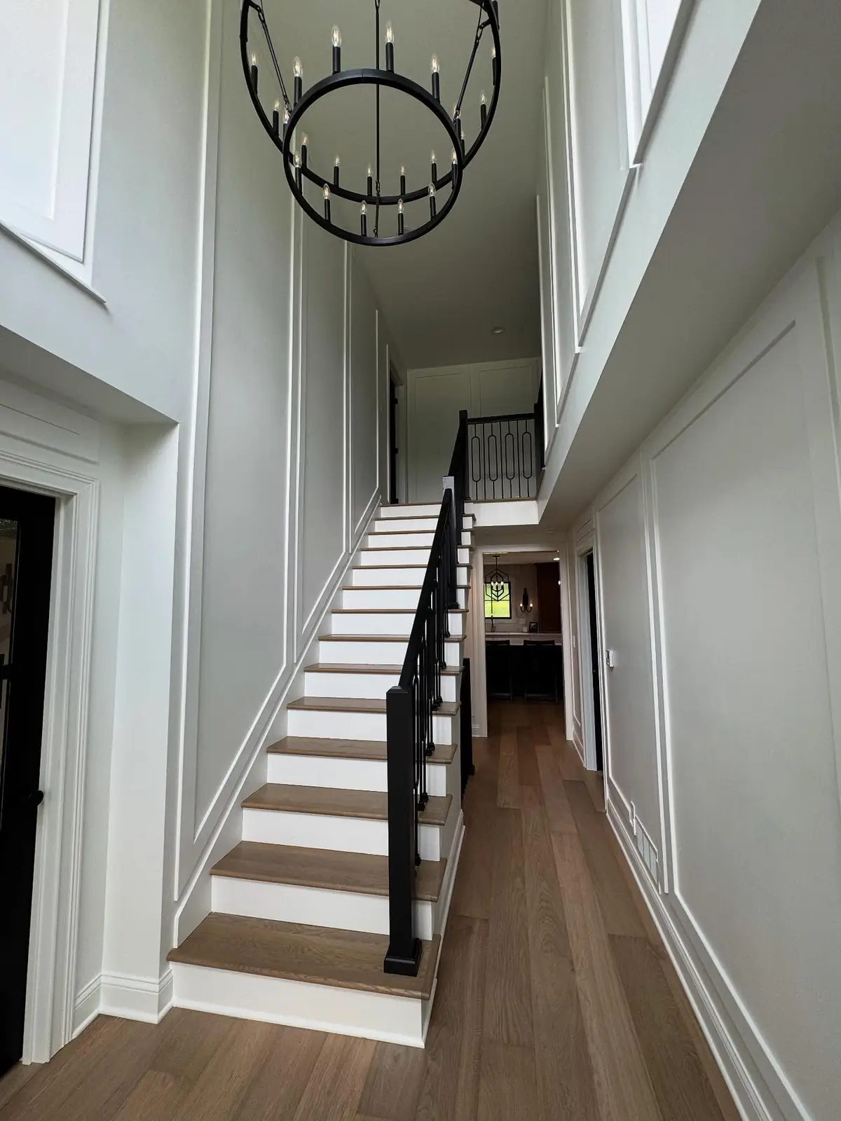 Renovated two-story staircase with black railing and iron chandelier