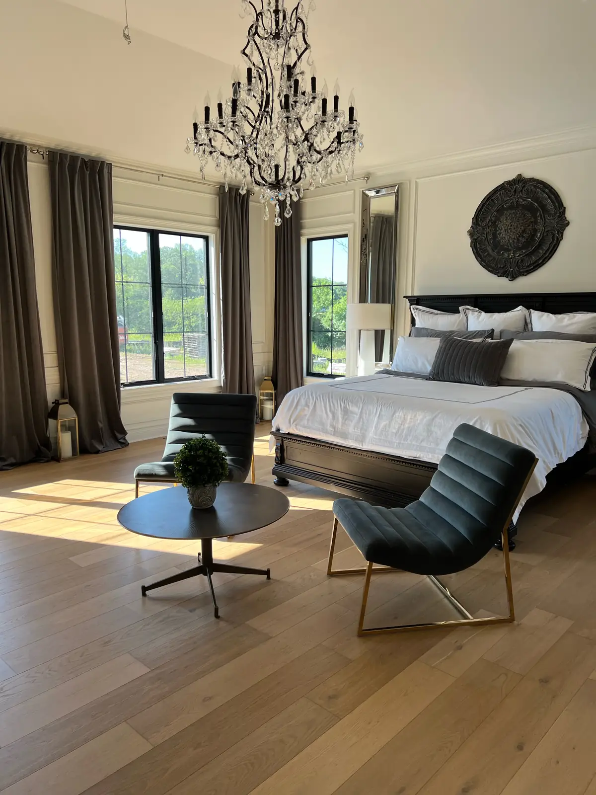 The primary bedroom from an angle, with a crystal chandelier and velvet chairs