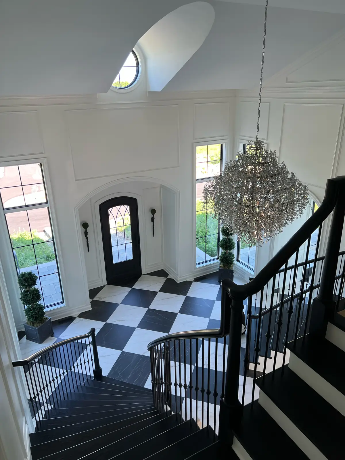 The foyer from the curved stair, beneath a crystal chandelier — French-Inspired Residence