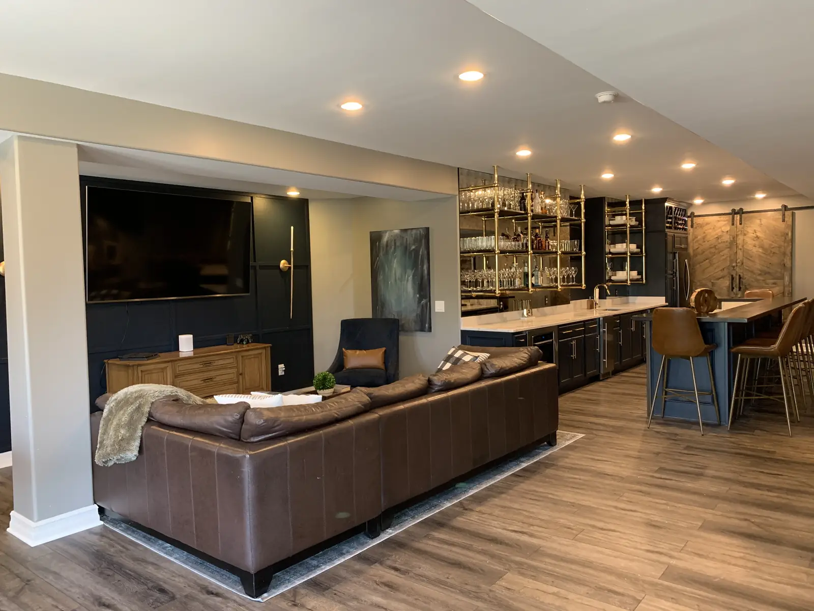 Indian Spring lower level: a leather sectional facing a navy TV wall, with the brass-shelved bar beyond