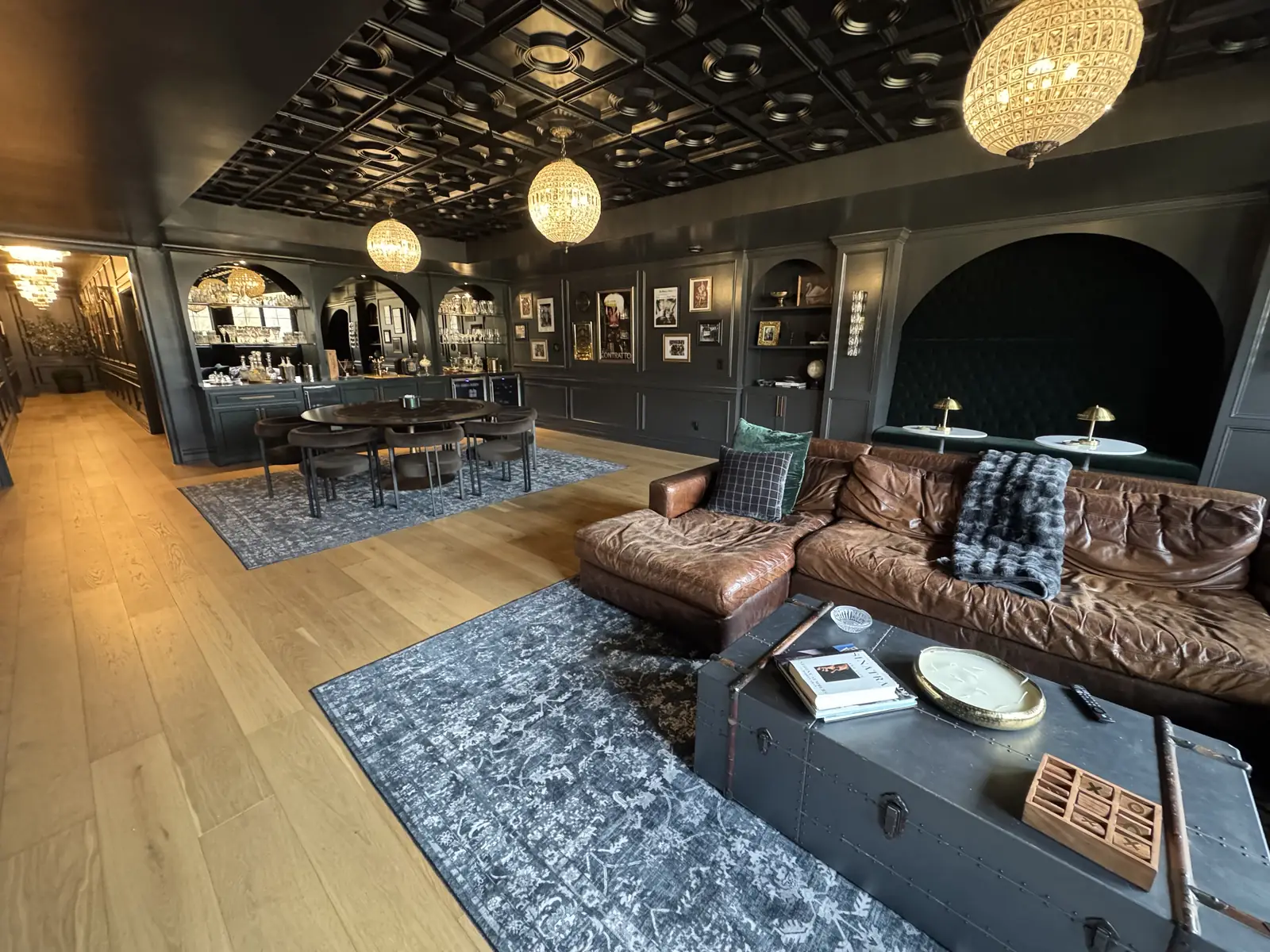 Speakeasy lounge with dark green paneling, globe chandeliers and a leather sectional — The Speakeasy Residence