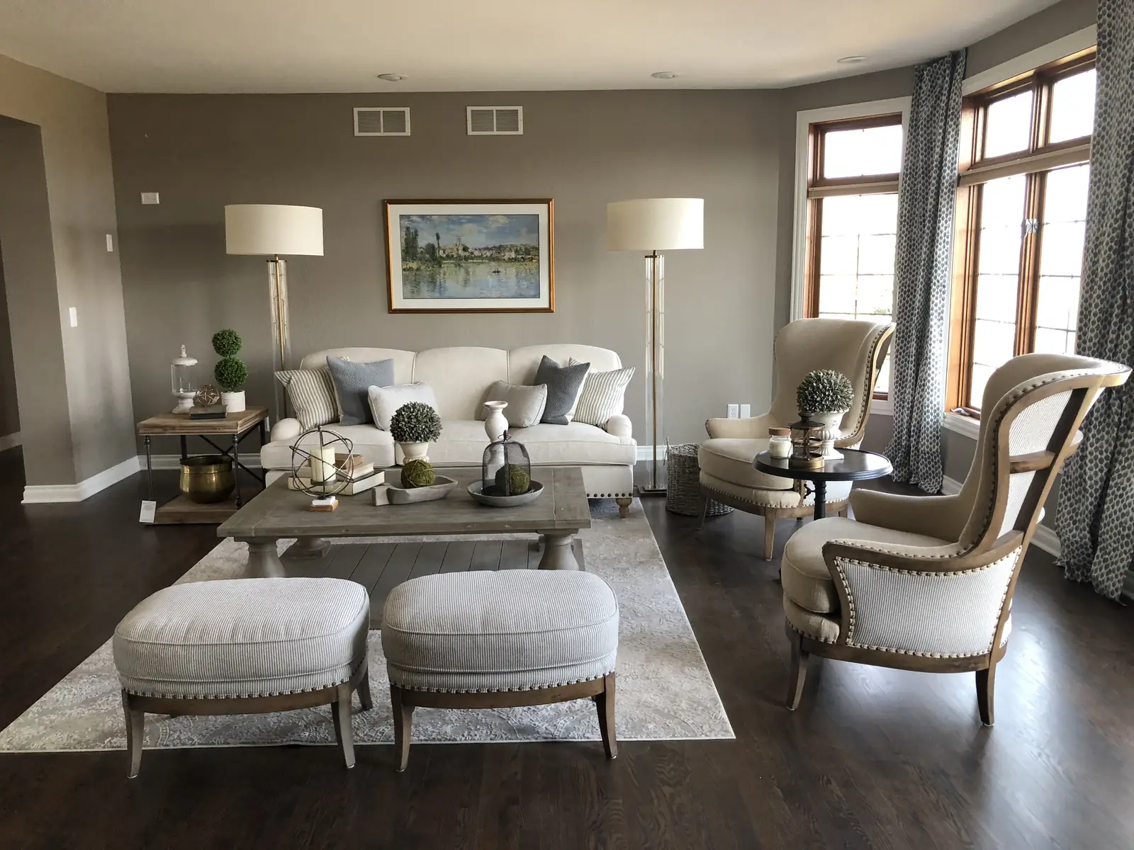 Living room after — soft neutrals, paired ottomans and dark wood floors