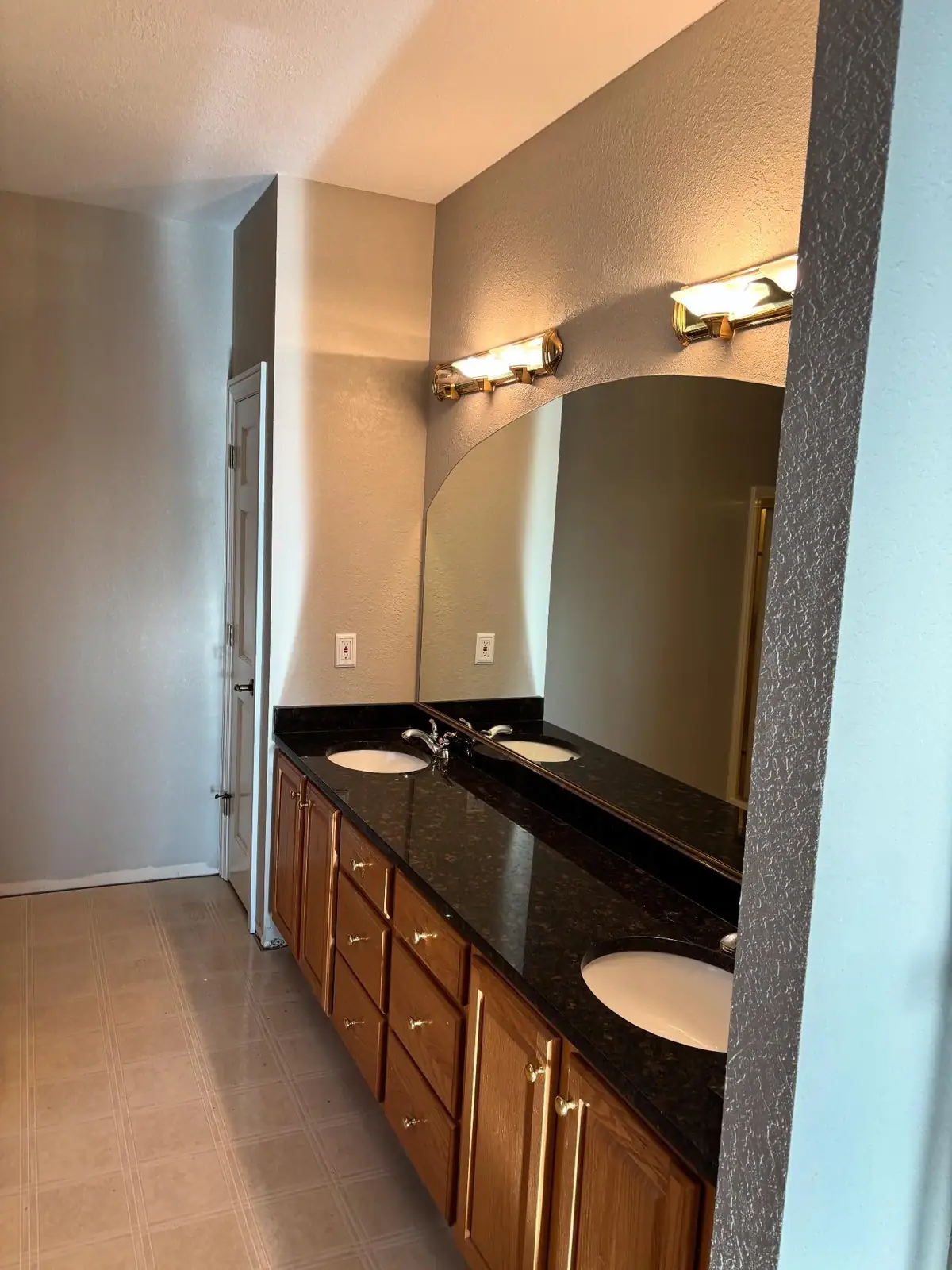 Primary bath vanity before — oak cabinets and black granite