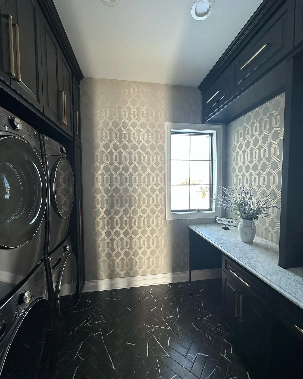 Stacked laundry in dark cabinetry over black herringbone tile, toward the window — French-Inspired Residence